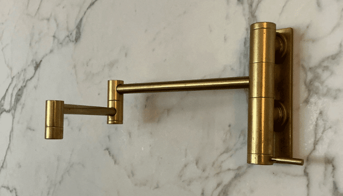 Close-up of a brass pot filler faucet mounted on a marble kitchen backsplash.